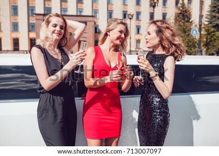 Beautiful women near a limousine drink champagne.