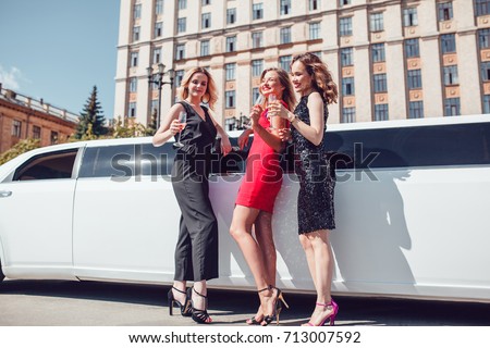 Beautiful women near a limousine drink champagne.