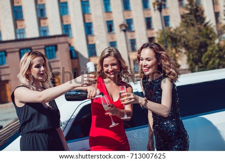 Beautiful women near the limousine have fun and drink champagne.