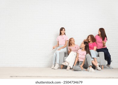 Beautiful women with pink ribbons sitting on sofa near white brick wall. Breast cancer awareness concept - Powered by Shutterstock