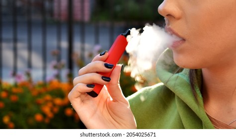 mujeres hermosas fuman cigarrillos electrónicos en la calle
