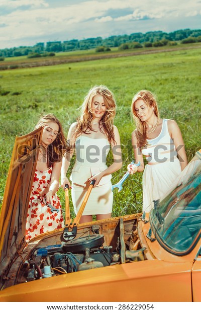 Beautiful women with tools are repairing a car on
the rural road