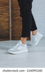 Beautiful Women's Shoes With Legs, Leather White Sneakers, In The Interior Of A Room Or Office, Shoes For A Woman, Black Trousers And White Sneakers, Casual And Modern Style, Modern And Trendy