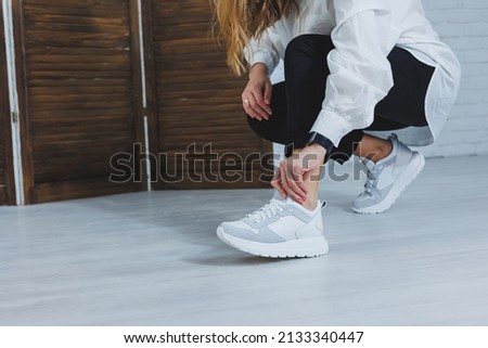 Beautiful women's shoes with legs, leather white sneakers, in the interior of a room or office, shoes for a woman, black trousers and white sneakers, casual and modern style, modern and trendy
