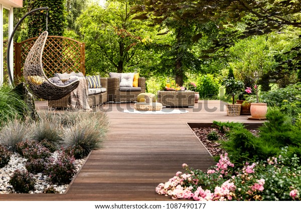 Beautiful wooden terrace with garden\
furniture surrounded by greenery on a warm, summer\
day