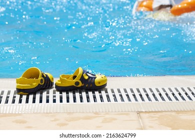 Beautiful, yellow, children's slippers are standing by the pool with blue water and an empty inflatable circle. The concept of an accident, drowning in water.