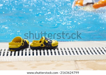 Beautiful, yellow, children's slippers are standing by the pool with blue water and an empty inflatable circle. The concept of an accident, drowning in water.