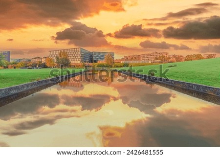 Beautiful yellow sunset with clouds over a river channel with reflection in a park overlooking residential buildings and a metro station DR Byen in the city area Ørestad. Copenhagen, Denmark