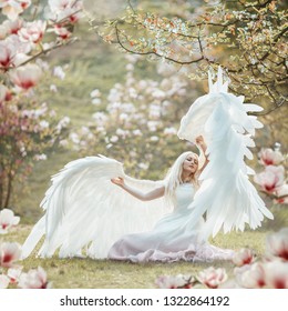 Beautiful yound woman with giant white angel wings posing in blooming magnolia garden.