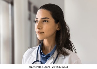 Beautiful young 30s Latina therapist or cardiologist, head shot portrait. Serious pensive Brazilian medical worker wear lab coat gazing away, deep in thoughts, pondering, looks thoughtful. Medicine - Powered by Shutterstock