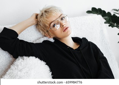 Beautiful Young Adult Blonde Woman In Black Hoodie On The White Sofa