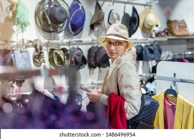 Beautiful Young Adult Caucasian Bald Woman Choosing And Trying On Hat In Department Retail Store At Shopping Mall. Portrait Of Happy Girl During Shopping