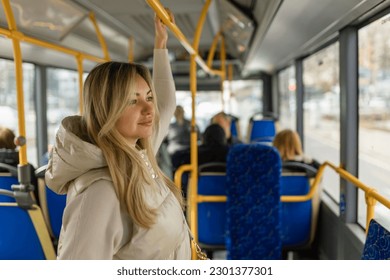 Beautiful young adult caucasian woman stands in the bus and looks into the distance