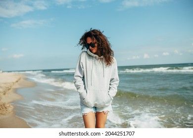 Beautiful young adult woman in gray blank hoodie or sweatshirt and sunglasses at the tropical beach. Mock-up for print. Space for your logo or design. - Powered by Shutterstock