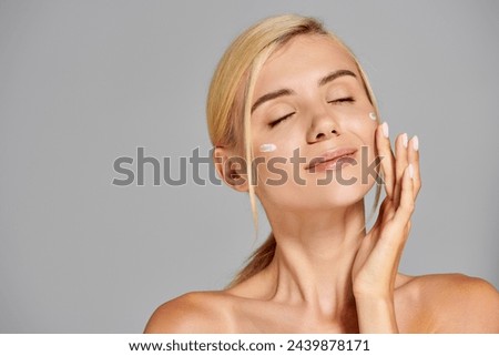 beautiful young adult woman with long earrings enjoying skin care against gray background