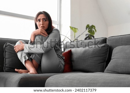 Beautiful young afraid woman sitting on sofa in living room
