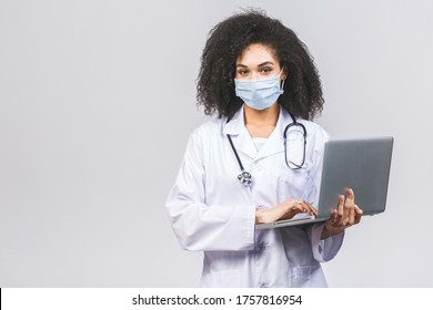 Beautiful Young African American Black Woman Doctor Or Nurse Isolated Over White Or Grey Background. Using Laptop Computer.