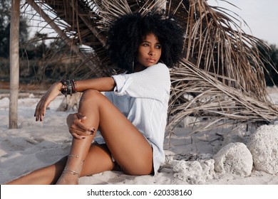 beautiful young african american girl sitting on sand at the beach