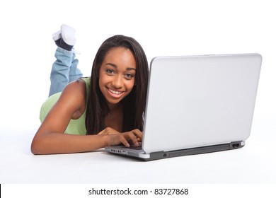 Beautiful young African American teenager girl lying on the floor enjoying surfing the internet on laptop with a happy smile.