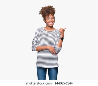 Beautiful young african american woman wearing glasses over isolated background smiling with happy face looking and pointing to the side with thumb up.