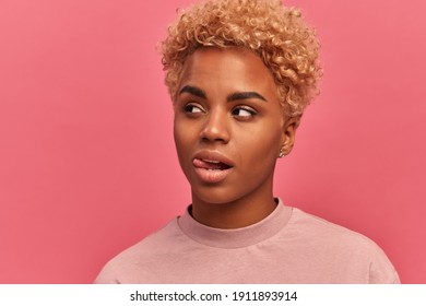 Beautiful young African American woman looks to side and sticks out her tongue with dreamy expression thinking about something tasty food standing on pink background. Concept of positive emotions. - Shutterstock ID 1911893914