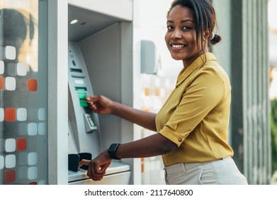 Beautiful young african american woman using an atm machine and a credit card while in the city