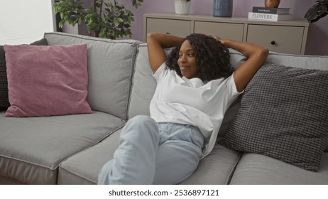 A beautiful young african american woman with curly hair relaxes on a sofa in a stylish living room, enjoying her indoor time in a comfortable home setting. - Powered by Shutterstock