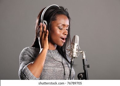 Beautiful young african american woman with eyes closed, wearing headphones and singing into microphone in recording studio.