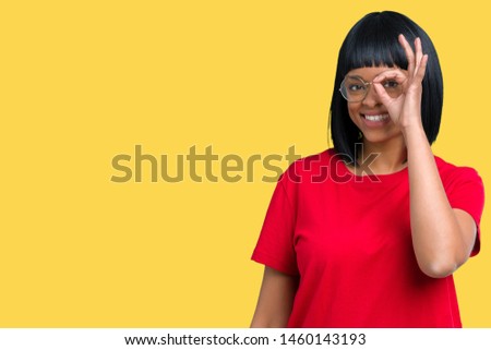 Beautiful young african american woman wearing glasses over isolated background doing ok gesture with hand smiling, eye looking through fingers with happy face.