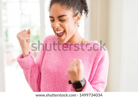 Beautiful young african american woman with afro hair excited for success with arms raised celebrating victory smiling. Winner concept.