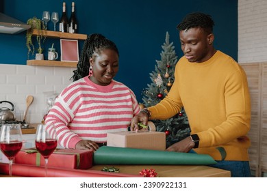 Beautiful young African couple wrapping Christmas gifts in colorful paper at home together - Powered by Shutterstock