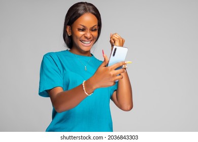 beautiful young african lady excited and rejoices while looking at her phone