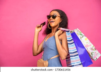 Beautiful Young African Lady Holding Shopping Bags And Credit Card Feeling Excited, Smiling, Colorful Photo Of Shopper