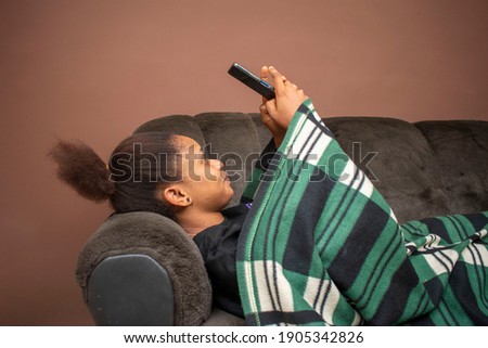 beautiful young african lady on a sofa online with her phone while covered with a blanket