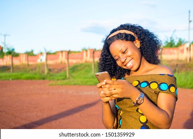 Beautiful Young African Lady Smiling While Using Her Phone Outdoors