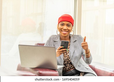 Beautiful Young African Muslim Business Woman Using Her Laptop Computer And Smartphone Smiling And Giving A Thumbs Up