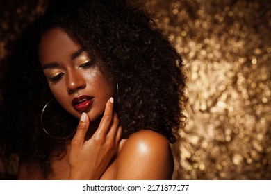 Beautiful young African woman with bright make up posing against a gold background.