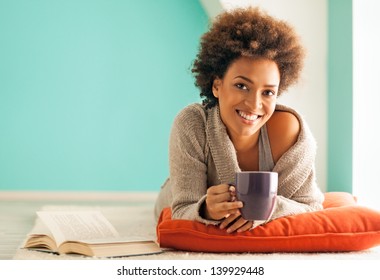 Beautiful young African woman enjoying a cup of coffee while relaxing at home. - Powered by Shutterstock