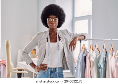 Beautiful young African woman leaning at the clothes rack while standing in the fashion design studio - Shutterstock ID 2040832178