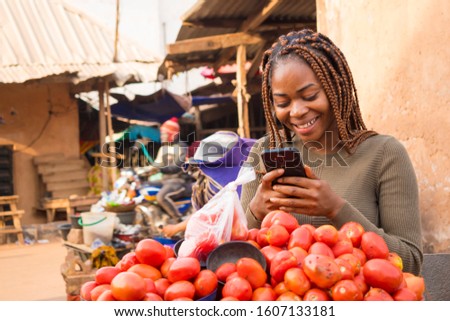 beautiful young african woman in a local african market viewing content on her phone smiling