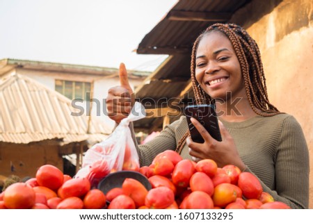 beautiful young african woman in a local african market using her smartphone giving thumbs up