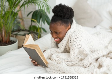 Beautiful Young African Woman Lying On A Bed Under A Blanket With A Book