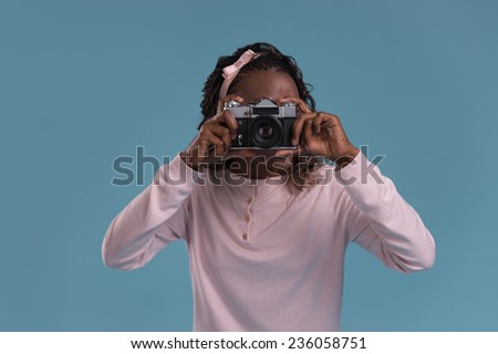 Beautiful young african woman using camera and photographing on blue background