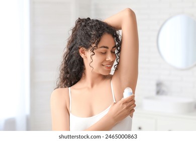 Beautiful young African-American woman applying deodorant in bathroom