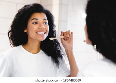 Beautiful young african-american woman brushing her teeth in the bathroom. African American woman look in mirror clean brush tooth in bathroom, young biracial female perform morning face care routine. - Powered by Shutterstock