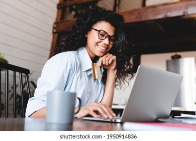 Beautiful young african-american woman buying online on laptop at home. African American woman look at laptop screen shopping online with credit card for payment. Happy young girl buy purchas.