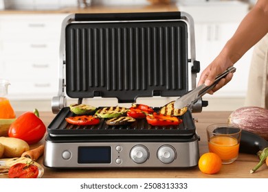 Beautiful young African-American woman cooking tasty vegetables on modern electric grill in kitchen, closeup - Powered by Shutterstock