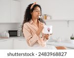 Beautiful young African-American woman eating ice cream in kitchen