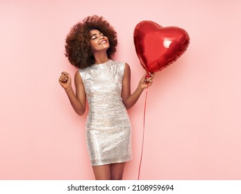 A beautiful young African-American woman with heart shape air balloon on a pink background. Woman on Valentine's Day. Symbol of love