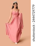 Beautiful young African-American woman in stylish pink prom dress and tiara on brown background